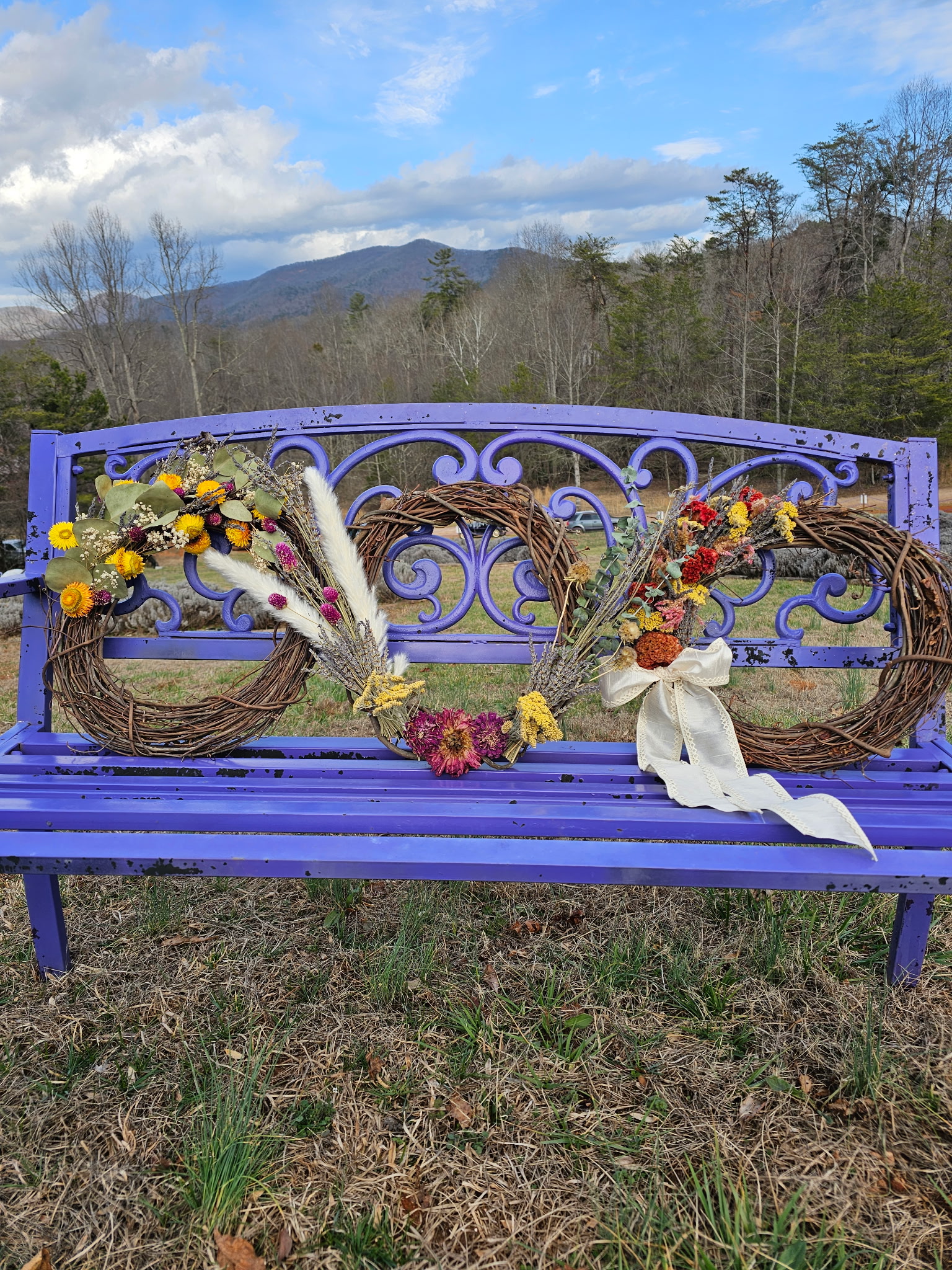 Dried flower wreaths on a lavender colored bench.